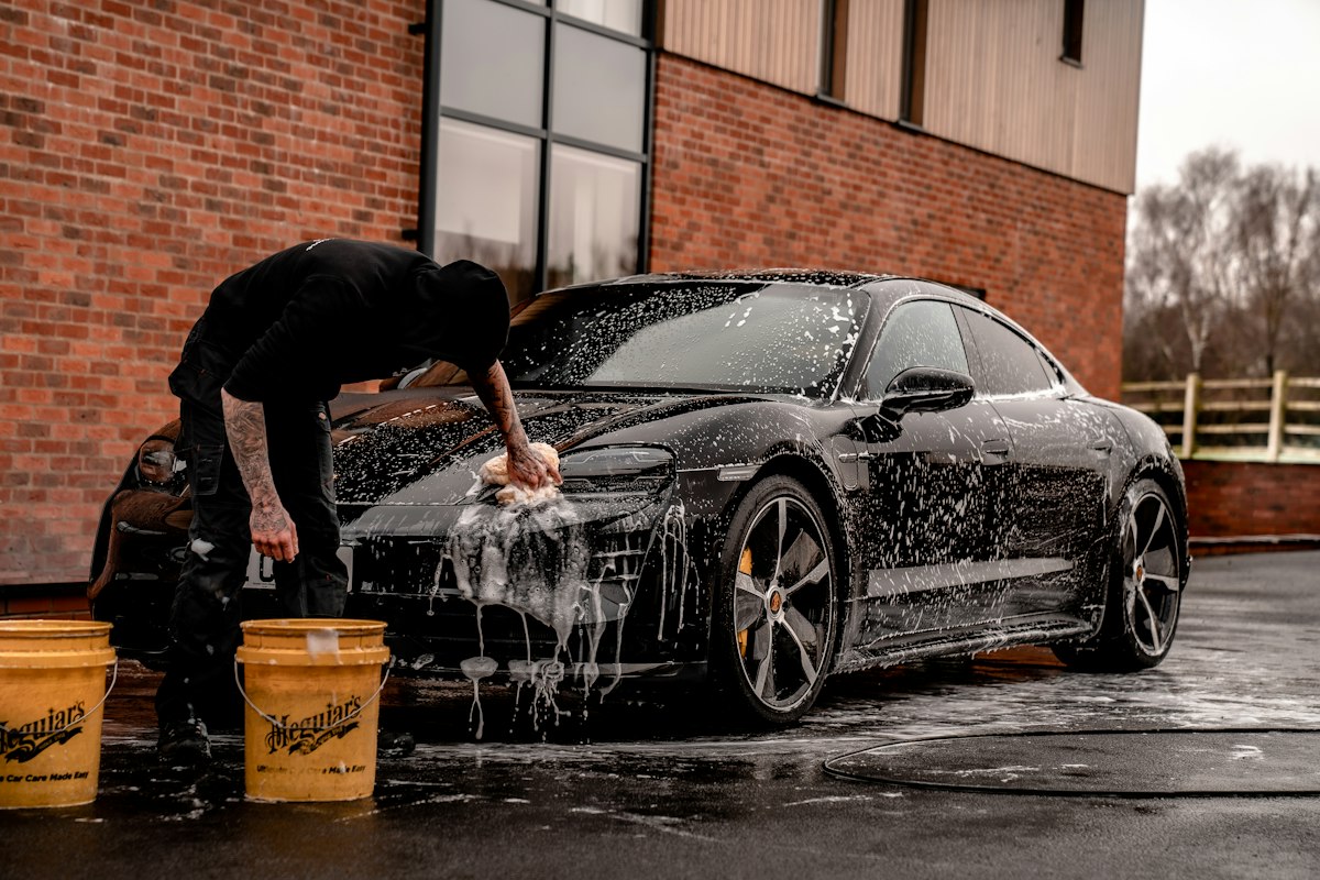 Hand-washing a black car covered in foam ahead of paint correction